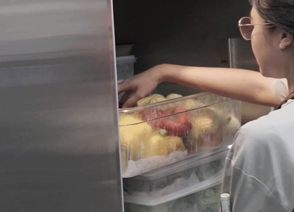 Seorang chef profesional sedang mengambil bahan makanan segar dari dalam unit pendingin stainless steel Solex di dapur komersial yang sibuk.